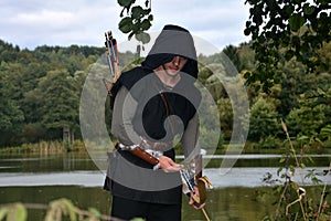 Medieval archer with black hood with the curve span before a lake and looks forwards photo