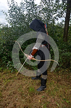 Medieval archer of the side stands with black hood and with tense bow and with arrow