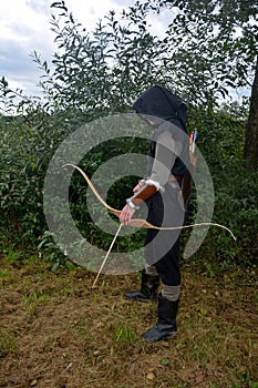 Medieval archer of the side stands with black hood and with tense bow and with arrow