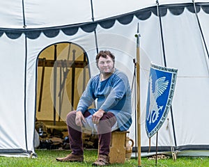 A medieval armorer sits outside his tent