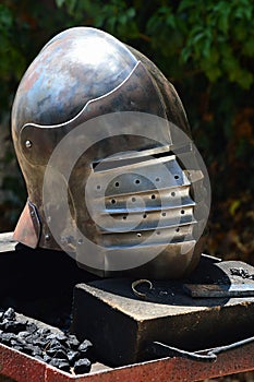 Středověká bascinetová přilba s odnímatelnou obličejovou maskou na pantu umístěném na zbrojařském pracovním stole