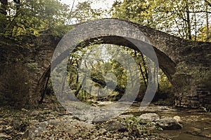 Medieval bridge over a river in a wooded setting in autumn