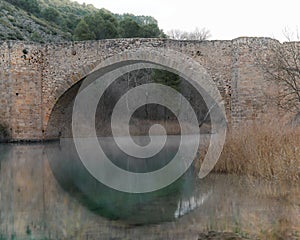 Medieval bridge reflected in the water in Spain over the river with fog photo