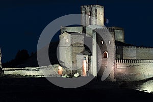 a medieval castle illuminated at night, highlighting its stone walls and towers against a dark sky