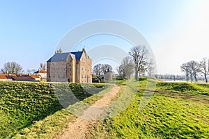 Medieval castle Slot Loevestein by earthen wall and moat at River Waal