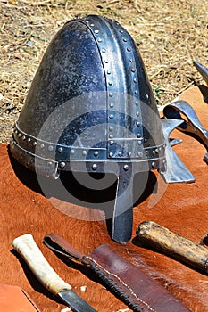 Medieval conical helmet also called norman casque with nosepiece displayed with knives and light battleaxe head displayed on orang