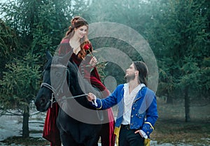 Medieval couple in love. man meets woman and gives rose in winter forest. Vintage clothing red long dress. Blue costume