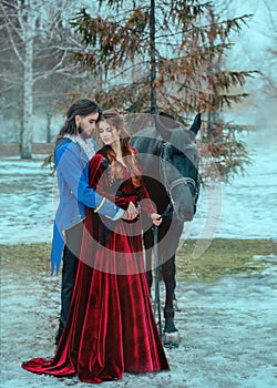Medieval couple in love man and woman hugging in winter forest. Vintage clothing red long dress. Blue frock coat costume