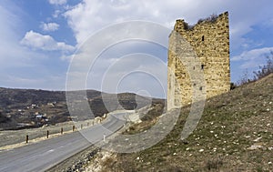 Medieval fortification stone tower near the road. Windows, loopholes and the village are visible. Blue sky with clouds