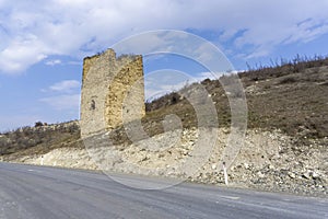 Medieval fortification stone tower near the road. Windows and loopholes are visible. Blue sky with clouds
