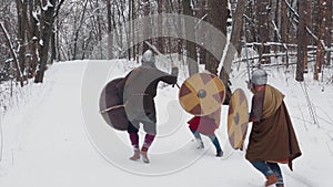 Medieval frankish, irish, viking warriors in armor fighting in a winter forest with swords shields