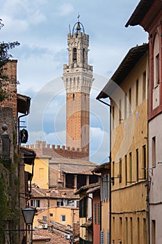 Medieval gothic bell tower Torre del Mangia of Palazzo Pubblico seen from the narrow streets of Siena old town