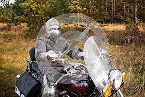 medieval knight in chainmail and a helmet with a sword in his hands sits on a motorcycle
