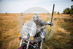 medieval knight in chainmail and a helmet with a sword in his hands sits on a motorcycle