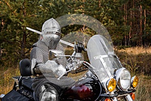 medieval knight in chainmail and a helmet with a sword in his hands sits on a motorcycle