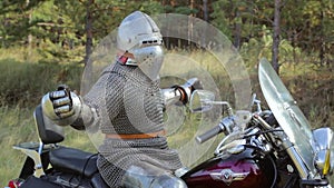 A medieval knight in full armor sits on a motorcycle against the backdrop of the forest