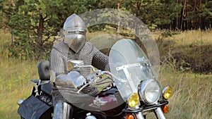 A medieval knight in full armor sits on a motorcycle against the backdrop of the forest