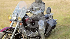 A medieval knight in full armor sits on a motorcycle against the backdrop of the forest