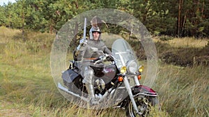 A medieval knight in full armor sits on a motorcycle against the backdrop of the forest