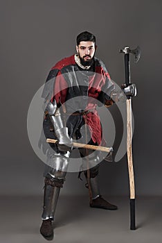 Medieval knight on grey background. Portrait of brutal dirty face warrior with chain mail armour red and black clothes
