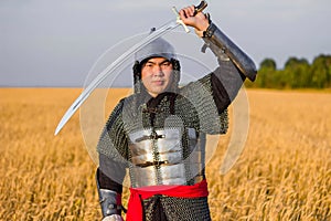 A medieval nomad warrior in oriental armor on the background of a wheat field. Standing in a fencing rack