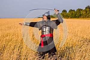 A medieval nomad warrior in oriental armor on the background of a wheat field. Standing in a fencing rack