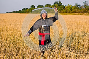 A medieval nomad warrior in oriental armor on the background of a wheat field. Standing in a fencing rack