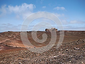 The medieval pirate fortress on the slope of a volcanic crater on the background of deep blue sky with white clouds