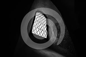 Medieval prison arch window with metal grid. Sunlight shining from the outside, dark, moody, low angle view, monochrome, no people
