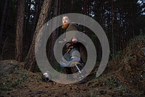 Medieval red-haired viking warrior with beard with two axes is preparing to attack on forest path