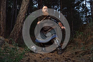 Medieval red-haired viking warrior with beard with two axes is preparing to attack on forest path