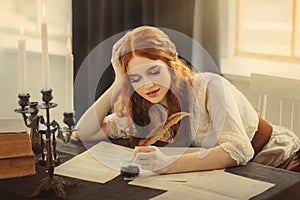 Medieval red-haired woman writer holds pen feather quill in hands, sits at table writes letter on sheet paper. Vintage photo