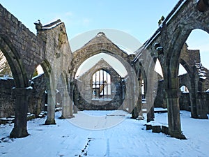 Medieval ruined church in heptonstall covered in snow showing arches and columns against a blue winter sky