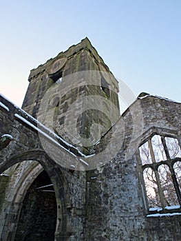 Medieval ruined church in heptonstall covered in snow showing arches and tower and windows against a blue winter sky
