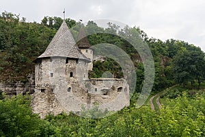 Medieval stone fort with two towers near the rock in the greenery. Kamianets-Podilskyi