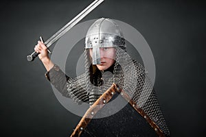 Medieval warrior in chain mail and a helmet with a sword and shields in his hands posing against a dark background