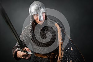 Medieval warrior in chain mail and a helmet with a sword and shields in his hands posing against a dark background