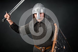 Medieval warrior in chain mail and a helmet with a sword and shields in his hands posing against a dark background