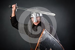 Medieval warrior in chain mail and a helmet with a sword and shields in his hands posing against a dark background