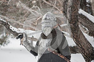 A medieval warrior dressed in chain mail, a steel breastplate and a helmet with a visor, armed with a sword and shield. The knight