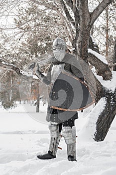 A medieval warrior dressed in chain mail, a steel breastplate and a helmet with a visor, armed with a sword and shield. The knight