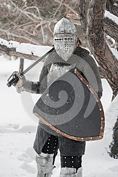 A medieval warrior dressed in chain mail, a steel breastplate and a helmet with a visor, armed with a sword and shield. The knight