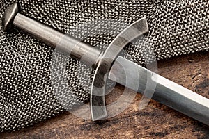 Medieval weapons and middle ages warfare conceptual idea with close up on sword on steel chain mail or maille on wooden background