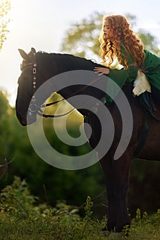 Medieval woman princess in green dress sits astride black steed horse.