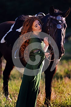 Medieval woman princess in green dress sits astride black steed horse.