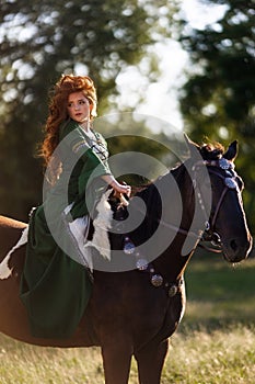 Medieval woman princess in green dress sits astride black steed horse.