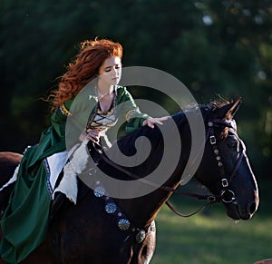 Medieval woman princess in green dress sits astride black steed horse.