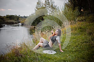 Medieval woman warrior in chain mail with a shield and a sword sits on the river bank in the evening