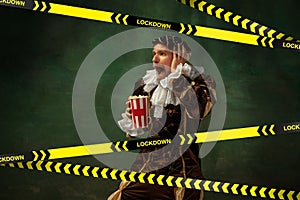 Medieval young man in old-fashioned costume with popcorn behing the limiting tapes with word Lockdown