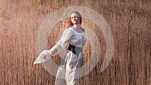 Medieval young woman in historical female costume at nature. Fantasy girl in white long dress or gown dancing at field